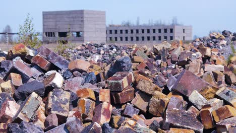 exterior view of abandoned soviet heavy metallurgy melting factory liepajas metalurgs territory, piles of debris and old bricks, distant brick buildings, sunny day, medium shot