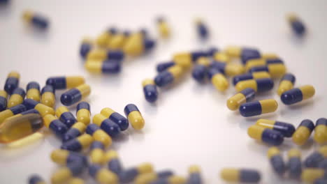 Macro-of-Blue-and-Yellow-Pills-Dropped-onto-One-Yellow-Pill-on-White-Background