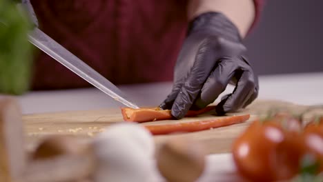 slow-motion of a chef preparing a red chili pepper for slicing. the sharp knife is ready to cut, with black gloves ensuring hygiene. fresh ingredients like tomatoes and herbs add depth to the scene