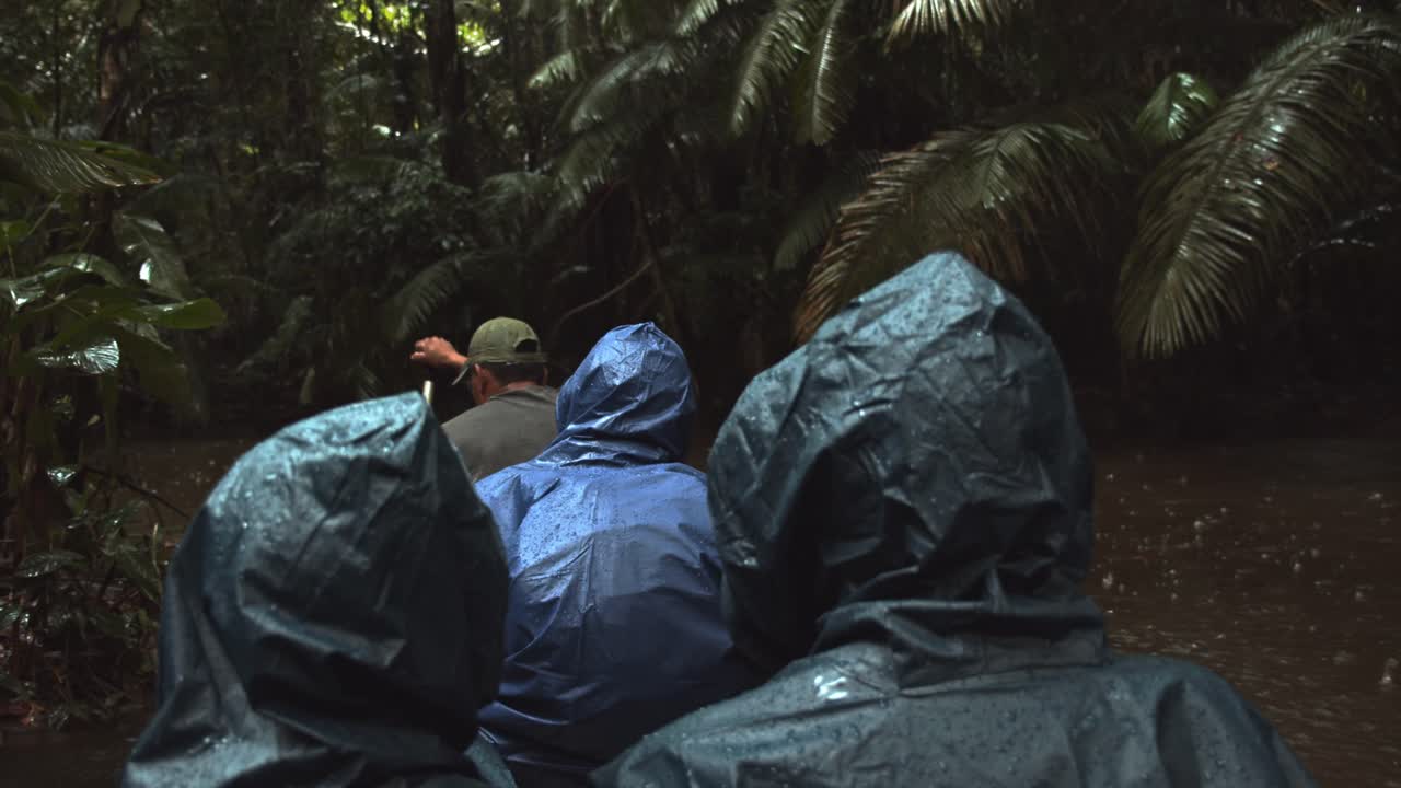 Tourist brave the rain on a boat in the rainforest as they navigate a narrow river