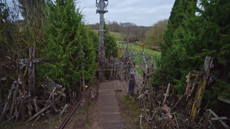 Walking-along-wooden-boardwalk-pass-worn-down-weathered-crosses,-art-display-of-devotion