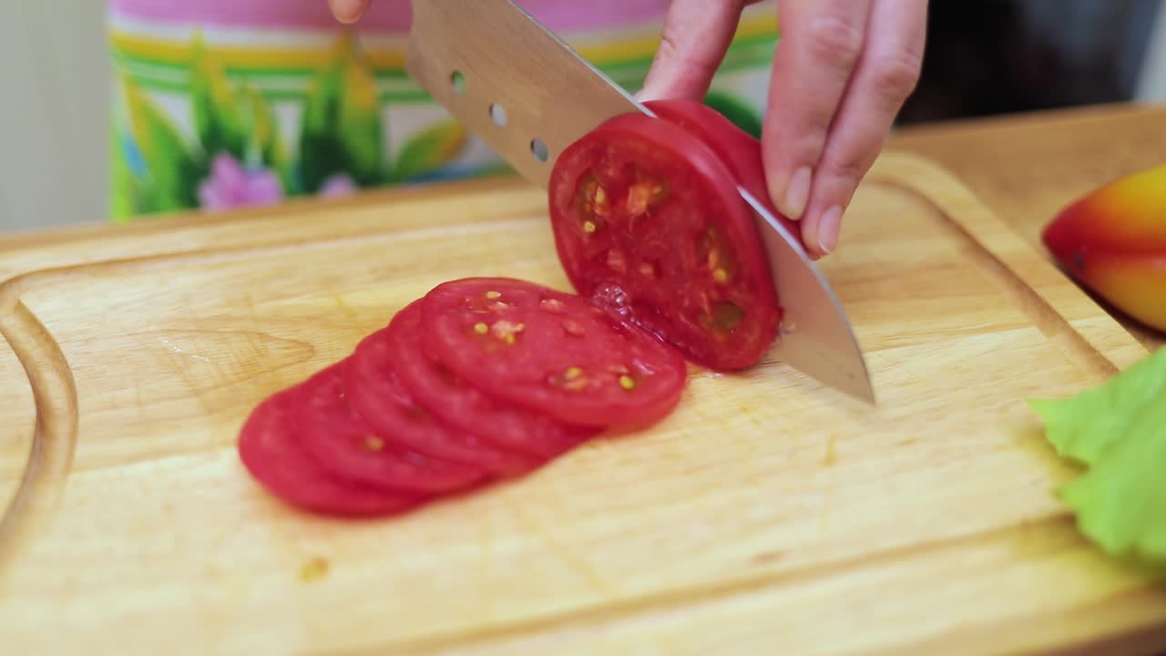 Women's hands Housewives cut with a knife fresh tomato on the cutting Board of the kitchen table
