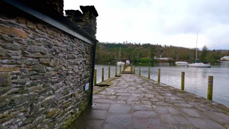 Lake-Windermere-Im-Englischen-Lake-District-Mit-Seinem-Ikonischen-Holzsteg,-Historischen-Steingebäuden-Und-Dem-Stimmungsvollen-Grauen-Himmel