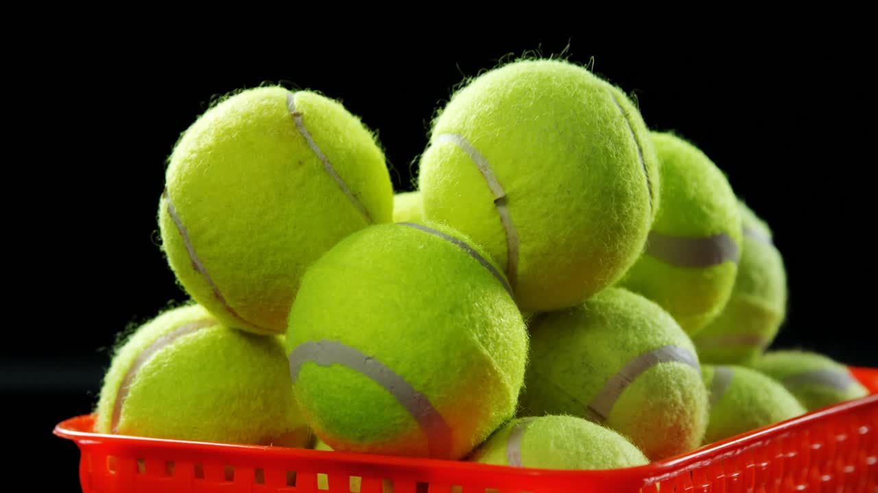 Korb voller Tennisbälle vor schwarzem Hintergrund