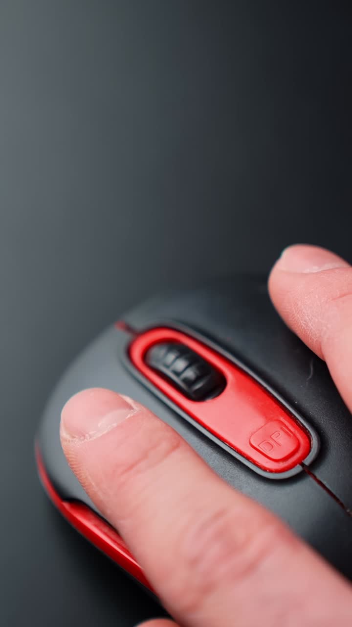 Vertical close-up of a hand clicking a red and black computer mouse on dark background with copy space, moody studio lighting