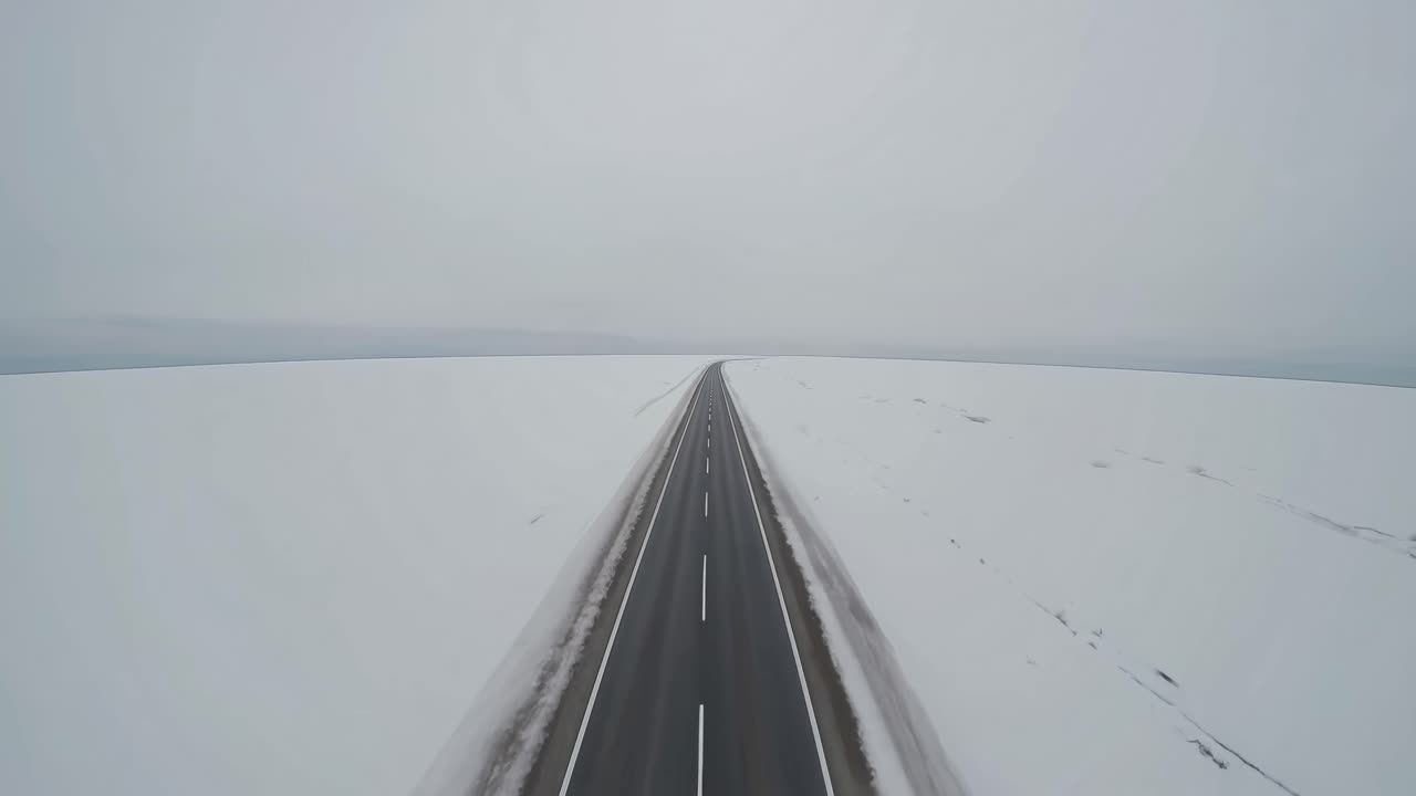 Aerial view of a straight road cutting through a vast snowy landscape, evoking a sense of solitude