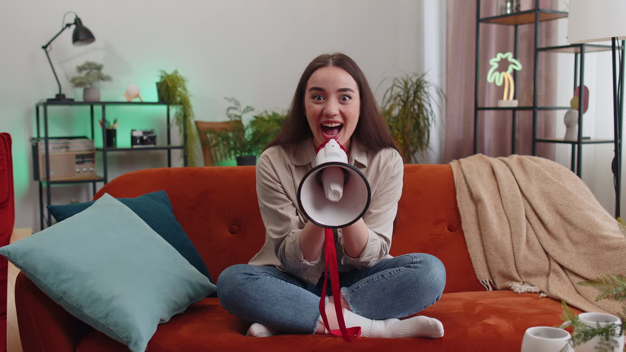 Young woman talking with megaphone proclaiming news loudly announcing advertisement at home room