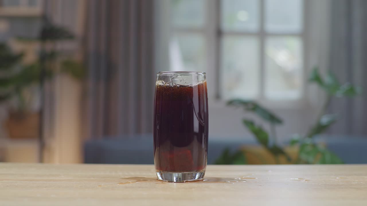 Cubetti di ghiaccio che cadono in un bicchiere di Coca-Cola fresca sul tavolo.