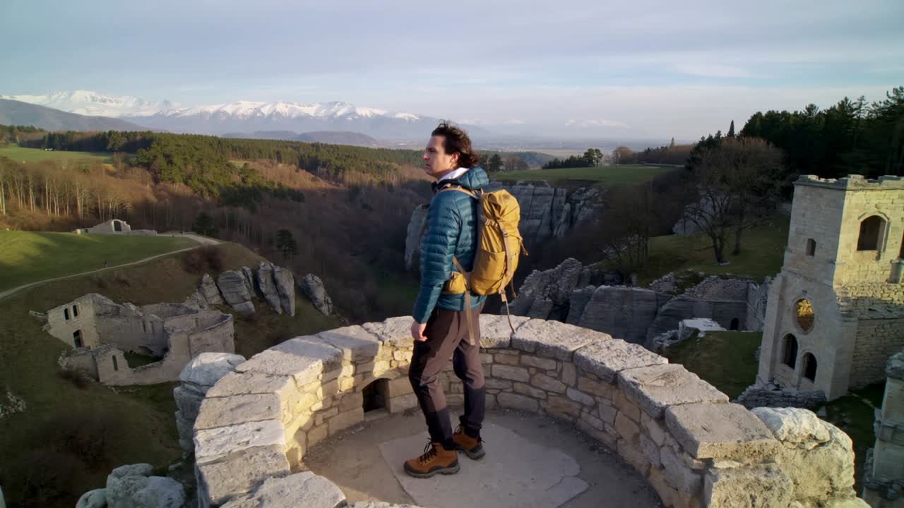 Escursionista in arrivo con giacca blu e zaino giallo in piedi su una torretta di pietra, che scruta la valle