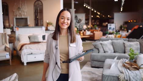 una joven madre profesional bien vestida mujer gerente de ventas mujer de negocios camina hacia la cámara sonriendo mirando hacia abajo feliz en el trabajo tecnología de tableta dispositivo de seguimiento en una tienda de muebles día de verano