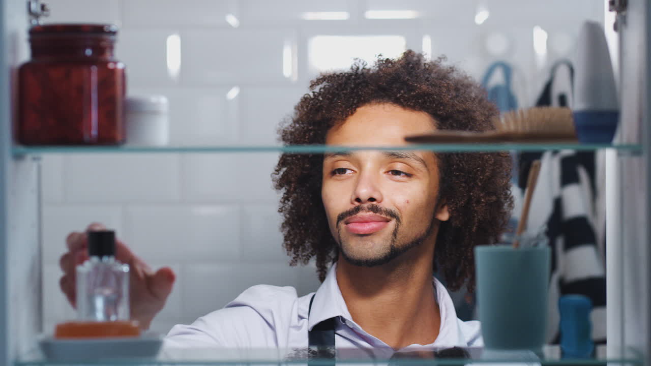 vista a través del gabinete del baño de un joven rociando colonia de la botella antes de ir a trabajar