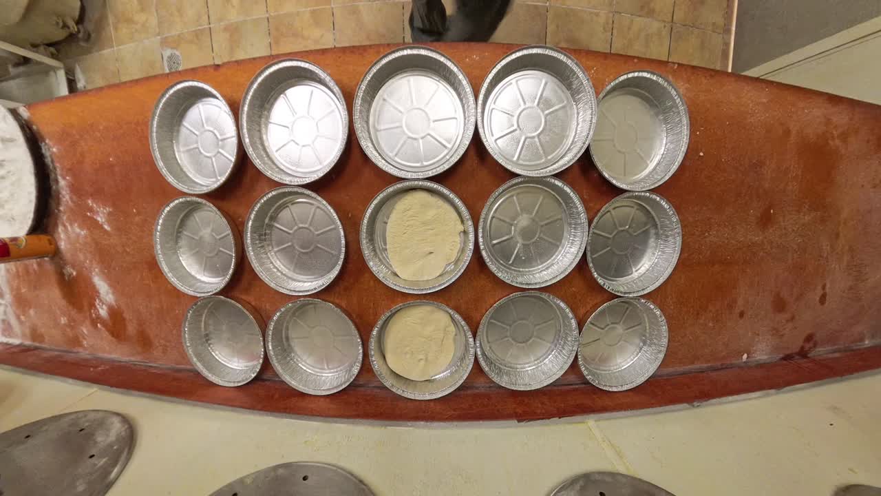 Raw pizza dough being placed in aluminum foil containers.