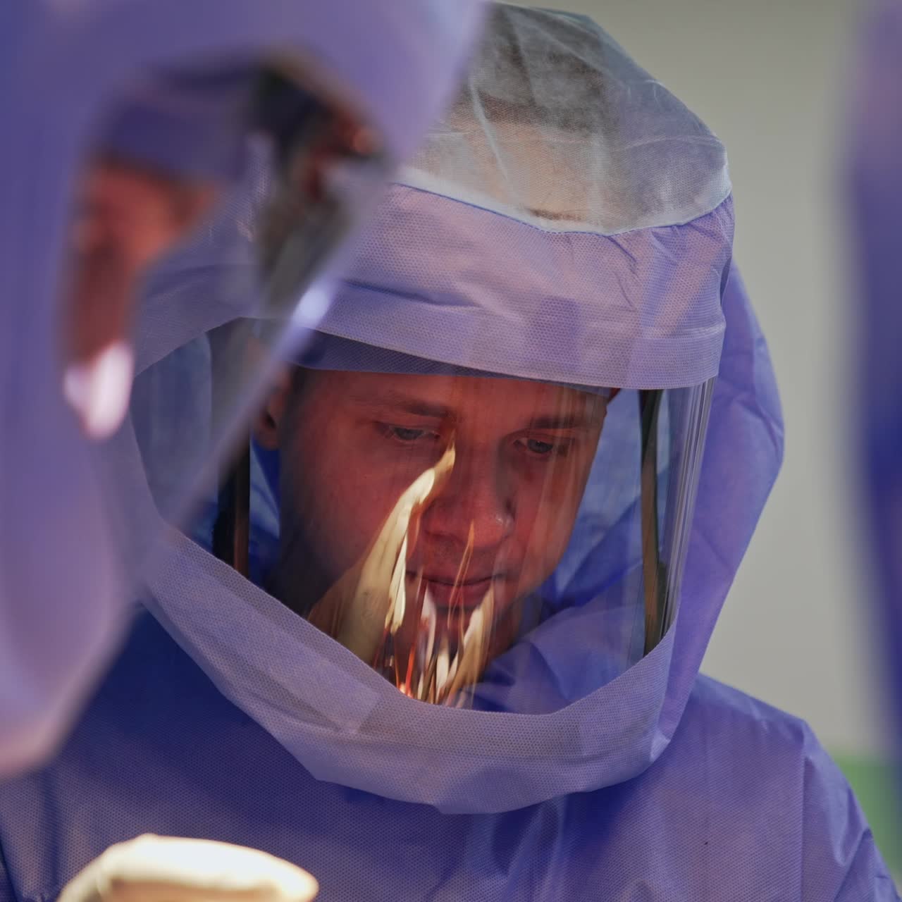 Calm focused face of a male surgeon in a protective suit during the surgery. Portrait of a doctor working in a surgical team in modern clinics