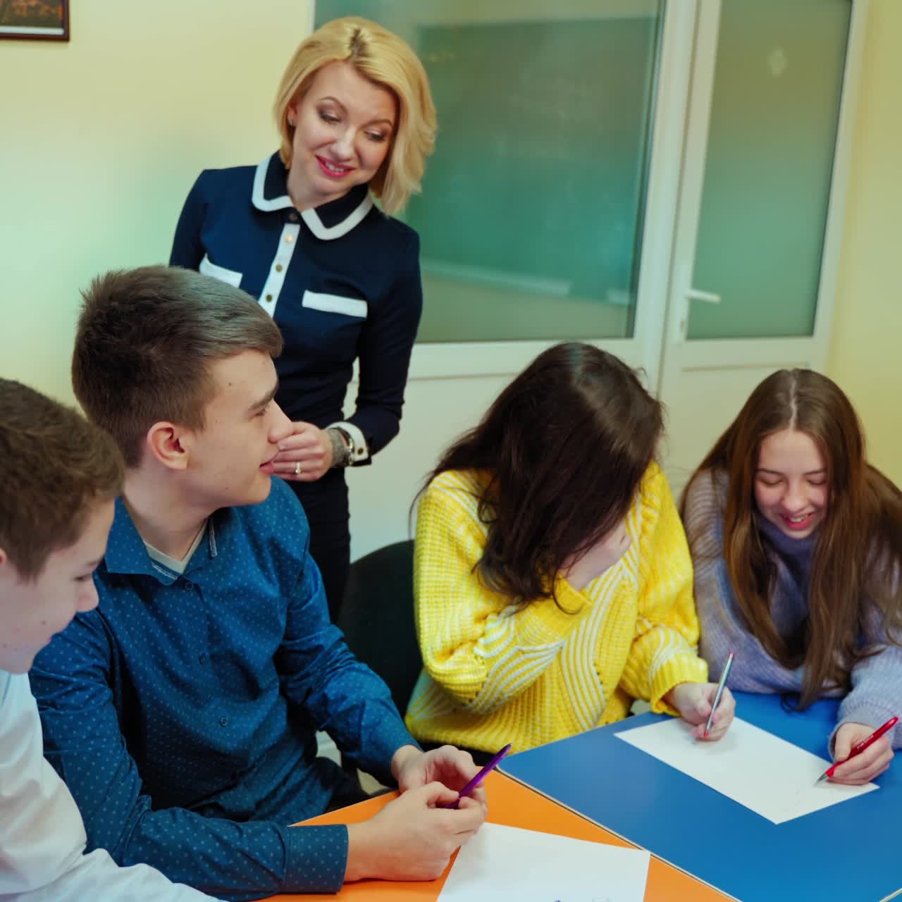 Female teacher talks with students. Teen pupils sitting in the classroom. Clever boy answering teacher questions at school.