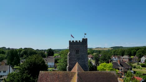 A-slow-ascending-boom-shot-of-St-Mary's-church,-with-Chartham-in-the-background,-and-a-union-flag-flying-from-the-tower