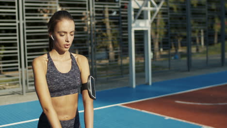 chica fitness con airpods haciendo sentadillas en la cancha deportiva en la mañana de verano