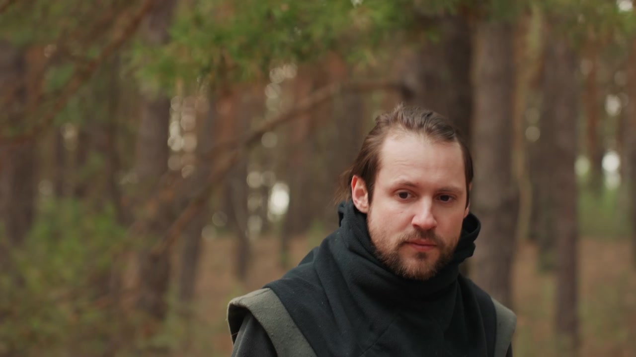 Ung kvinne og mann beveger seg langs en furuskogssti i mykt høstdagslys, med vindblåst hår, lagdelt strikketøy, rolige uttrykk og en mild pause som antyder ettertenksom utendørsreise.
