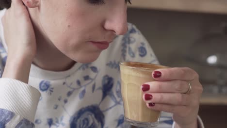 Young-beautiful-girl-drinking-flat-white-coffee,-picking-up-glass-from-a-wooden-table