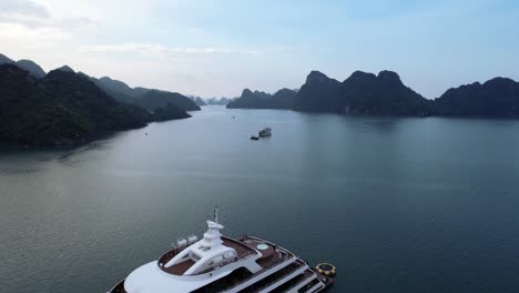 aerial drone flying over white luxury yacht anchored in ha long bay vietnam in tropical blue water at sunset