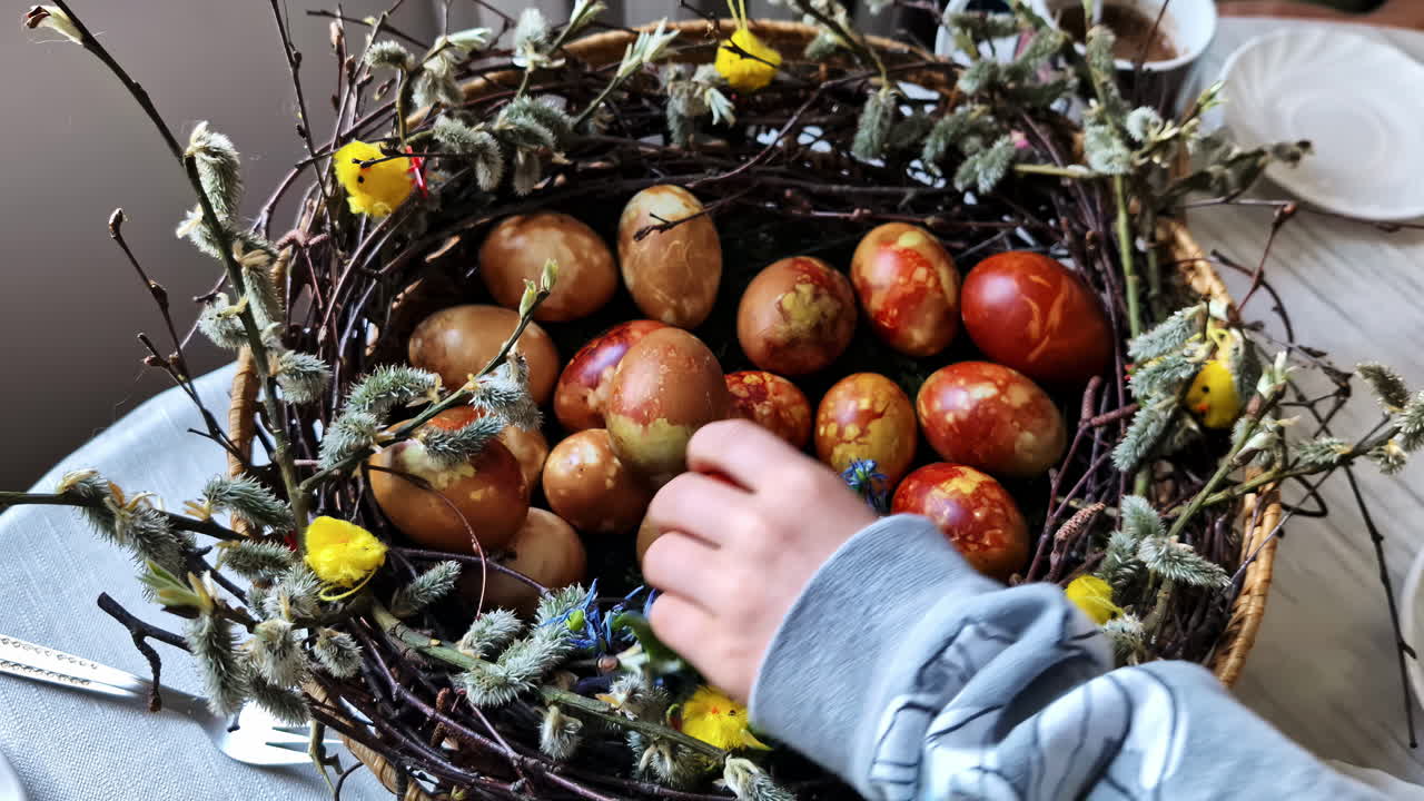 Child reaching for natural dyed Easter eggs in decorative woven nest basket