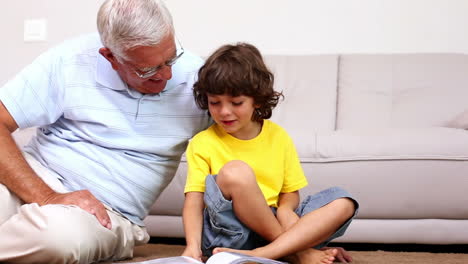 Senior-man-sitting-on-floor-with-his-grandson-looking-at-photo-album