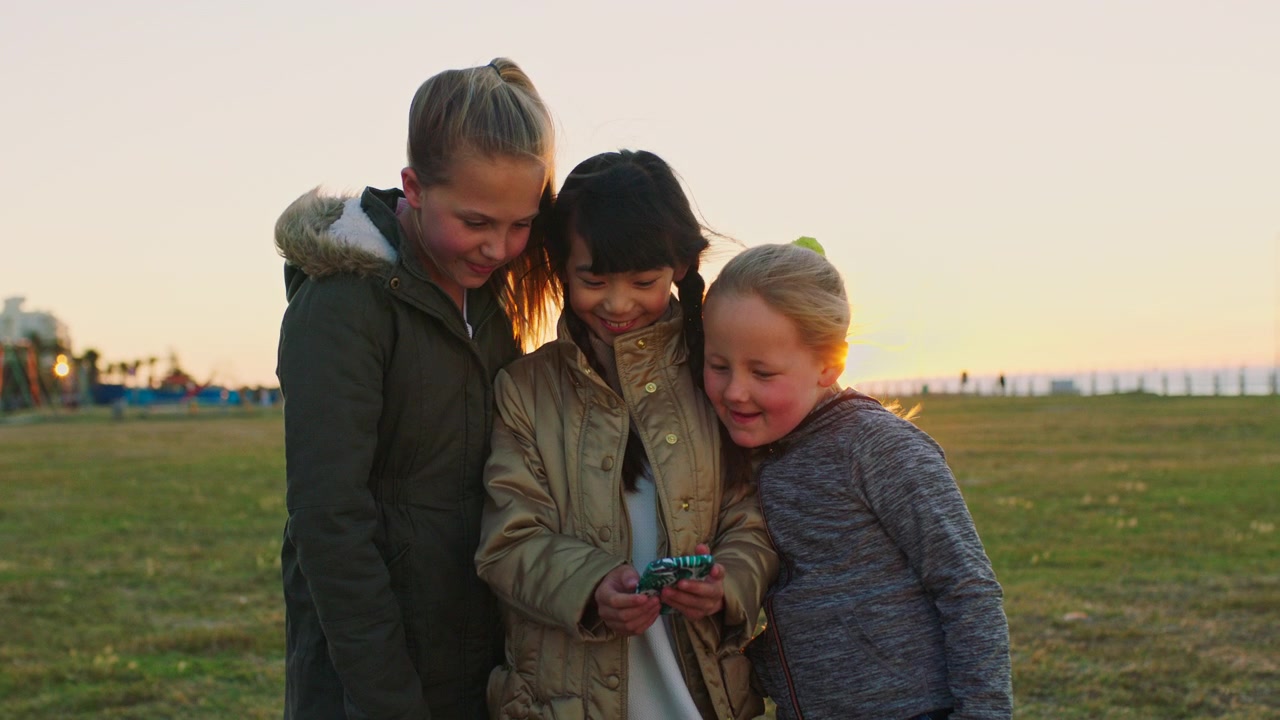 Tre giovani ragazze che guardano insieme uno smartphone all'aperto al tramonto