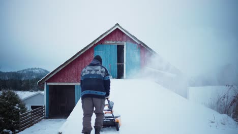 vista trasera de un hombre limpiando la nieve fuera de una granja en noruega