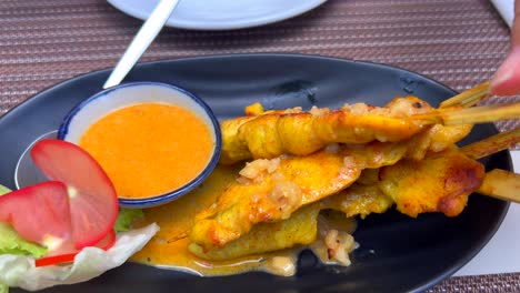 sumergir palitos tradicionales de pollo tailandés en salsa de maní en un restaurante, comida asiática sabrosa, tiro de 4k