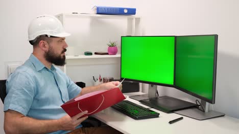 ingeniero con casco de seguridad o casco duro trabaja en una computadora, dos pantallas de monitor muestran pantallas verdes. trabajo remoto en casa