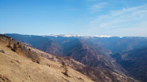 panoramic view of a mountain range with dry hills and snow-capped peaks under a clear blue sky