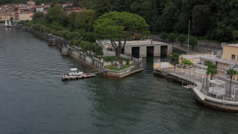 Drone-Alejándose-De-La-Gente-En-El-Muelle-Del-Lago-Como,-Italia