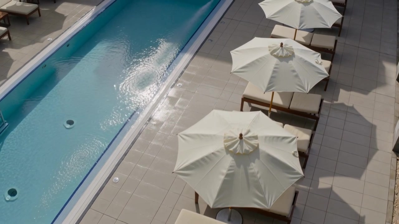 Panning camera revealing row of white umbrellas casting shadows at resort pool deck, copy space