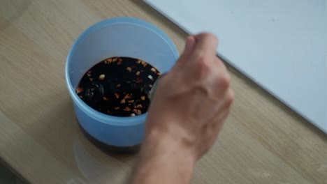 pouring sesame oil into soy sauce marinade mixture in plastic container. -closeup shot