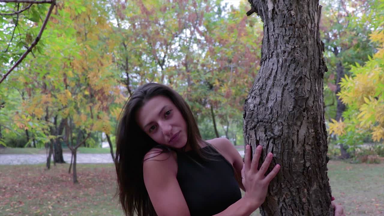 hermosa modelo femenina con cabello negro modelando cerca de un árbol en un parque