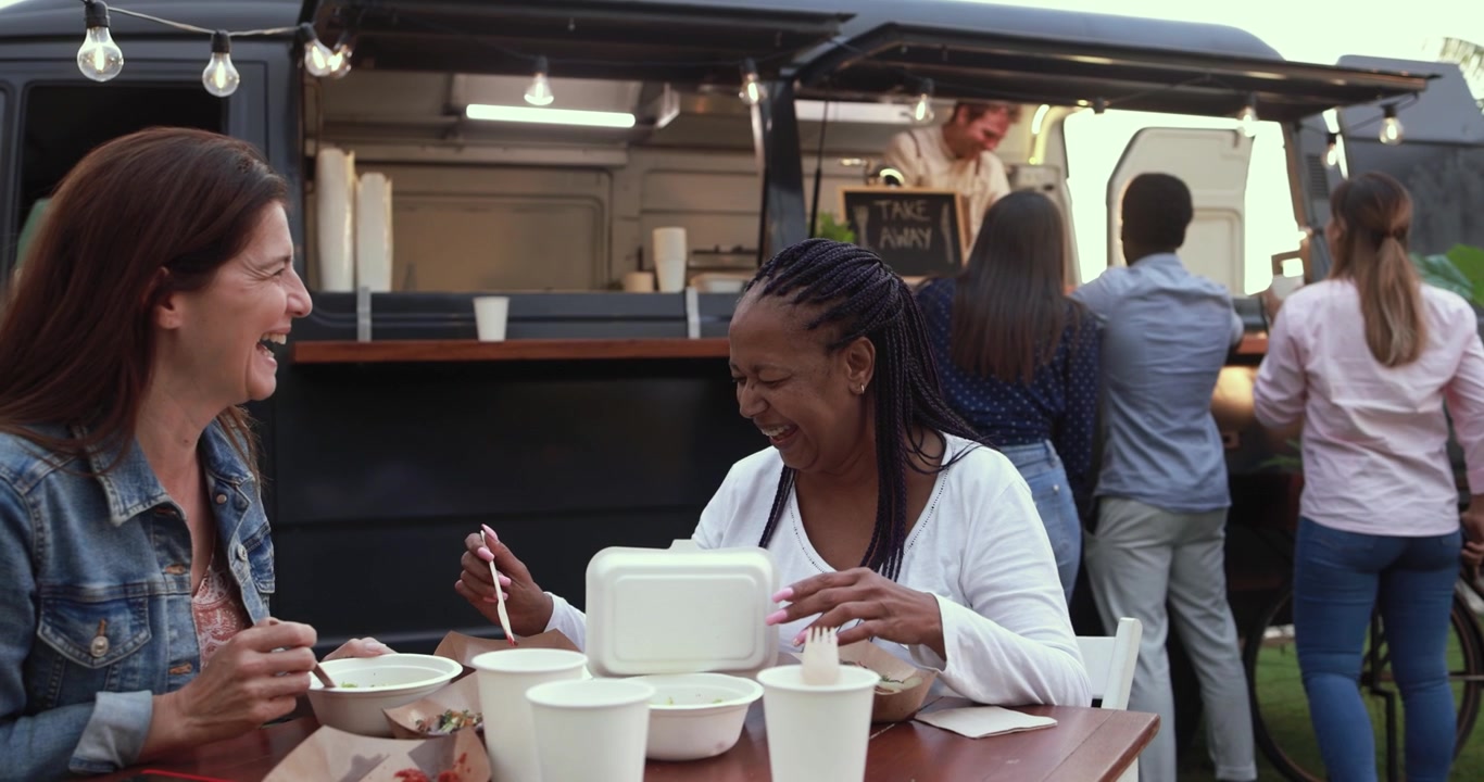 Glade, forskellige kvinder griner og spiser ved et udendørs food truck-arrangement