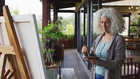 Senior-mixed-race-woman-painting-on-balcony