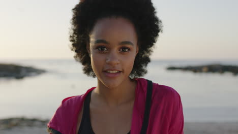 Porträt-Einer-Jungen-Athletischen-Afroamerikanischen-Frau,-Die-Fröhlich-Am-Ruhigen-Strand-Bei-Sonnenuntergang-Lächelt