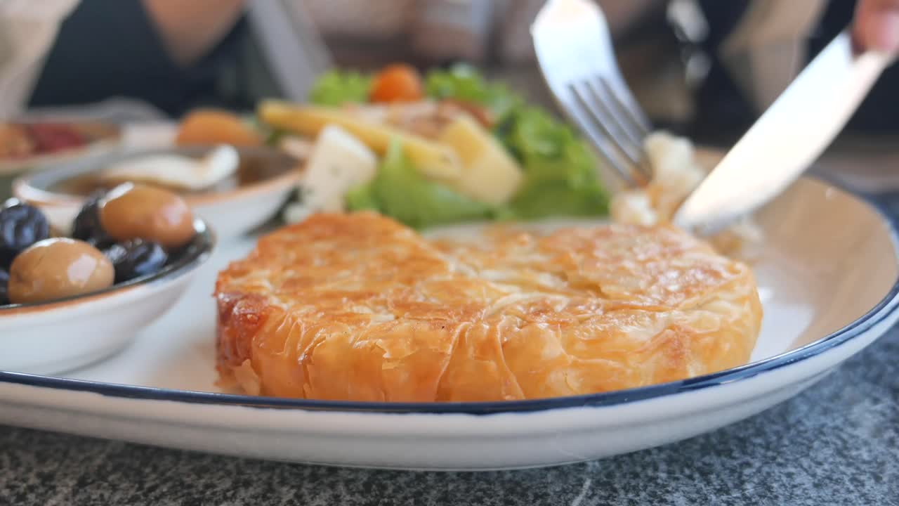 A plate of food with pastry, olives, cheese, and salad