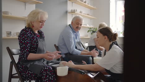 a young woman teaches a group of senior women and a man of 60-70 years old to pottery. activities for the elderly