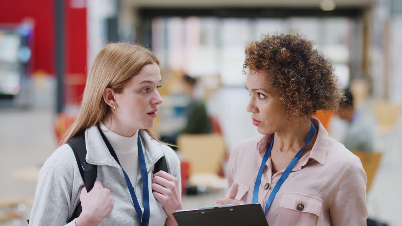 Female College Student Meeting With Woman Tutor In Busy Communal Campus Building