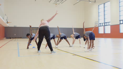 in school gym, students stretching with female teacher leading group exercise session