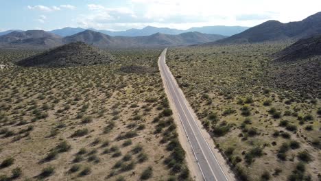 Aerial-shot-of-a-straight-road-in-the-middle-of-the-desert-with-blue-sky-and-hills