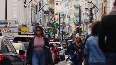 busy shoppers walk along rue d'antibes in cannes surrounded by stores and passing cars