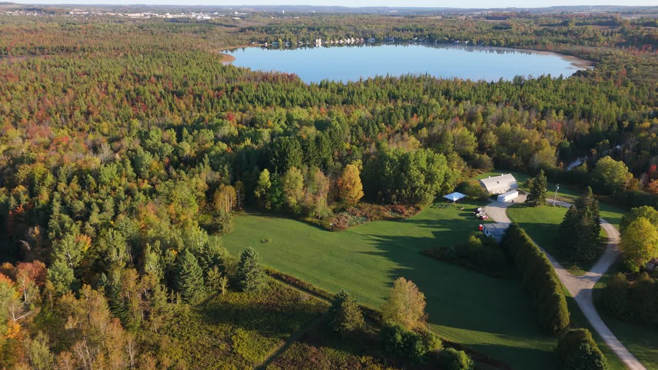 A stunning aerial view of a private lake in Caledon, Ontario, surrounded by a forest displaying spectacular peak fall colours on a beautiful sunny day