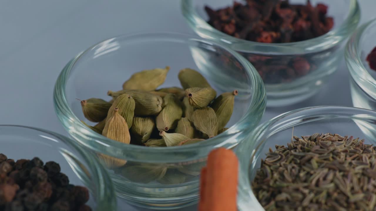 different types of whole spices Cinnamon stick, Black pepper, Caraway seed, green cardamom, dried red chilli and Cloves in small glass bowl, 4k, parallax shot.