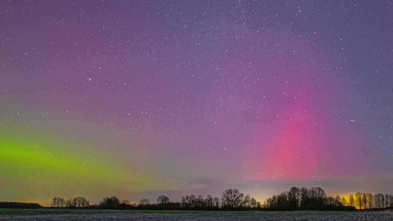 Colorful time lapse of the Northern Lights (Aurora Borealis) in green and pink under a purple starry sky with moving stars above a field and trees