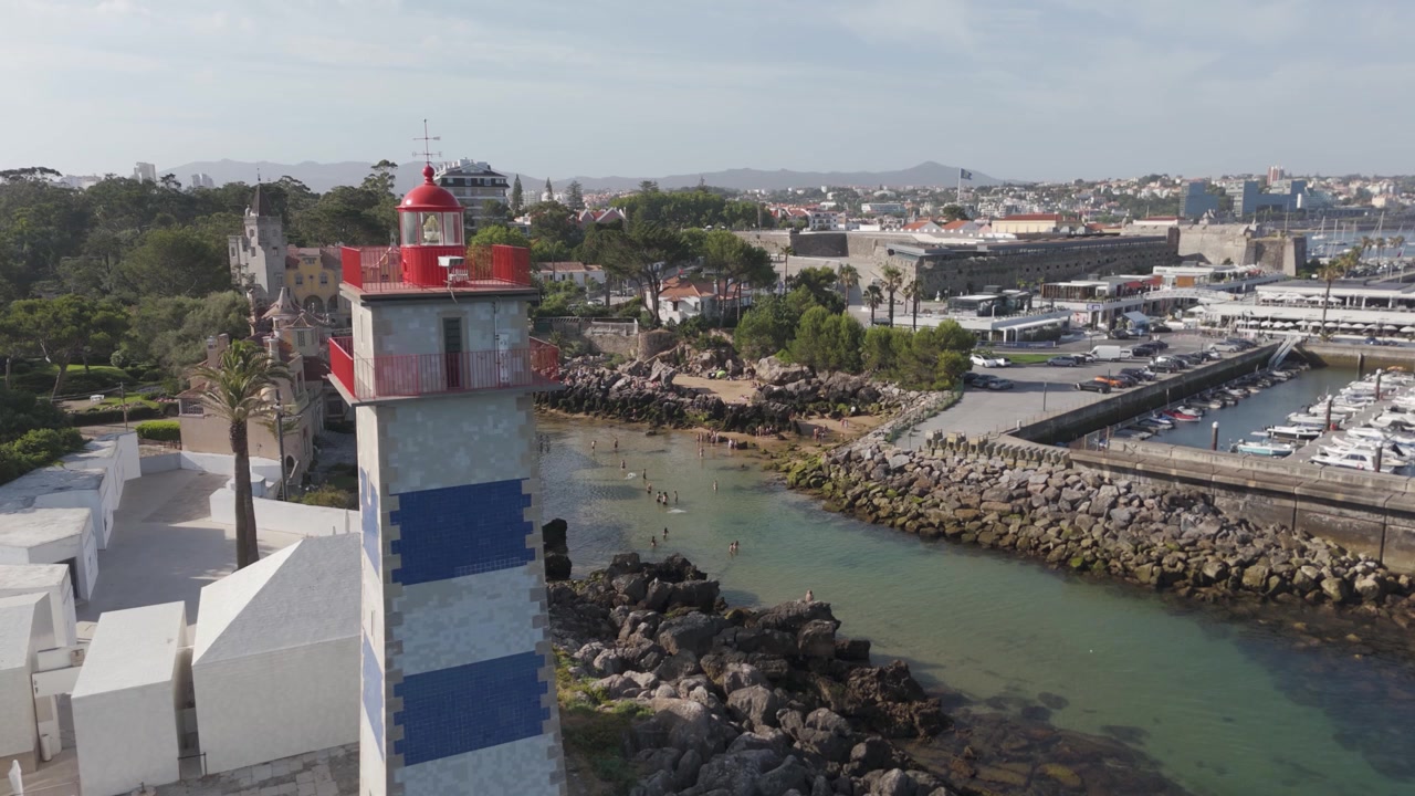 Drone view showing santa marta lighthouse, the coastal town of cascais, and a bustling marina with boats under a clear sky