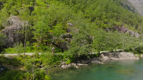 couple hiking in mountain woodland with flowing river, aerial fly towards view