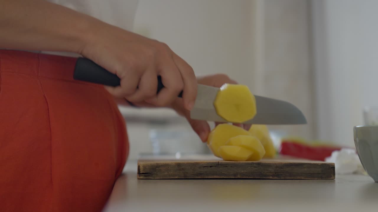 estática, primer plano de una mujer cortando patatas con un cuchillo de chef en una pequeña cocina durante el mediodía