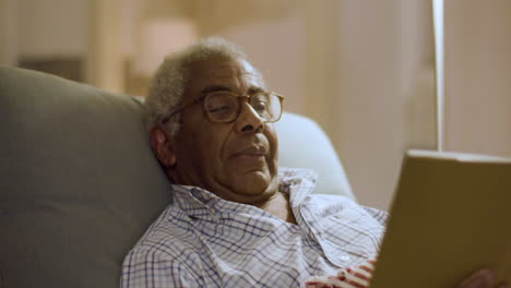 closeup of elderly black man reading hardcover book lying in bed